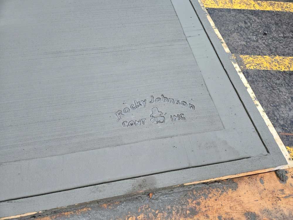 Sidewalk corner with faint graffiti near a curb and painted road markings.