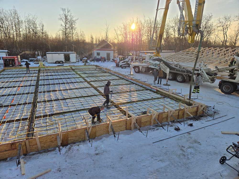 Construction site with workers pouring concrete over a rebar grid at sunrise in winter.