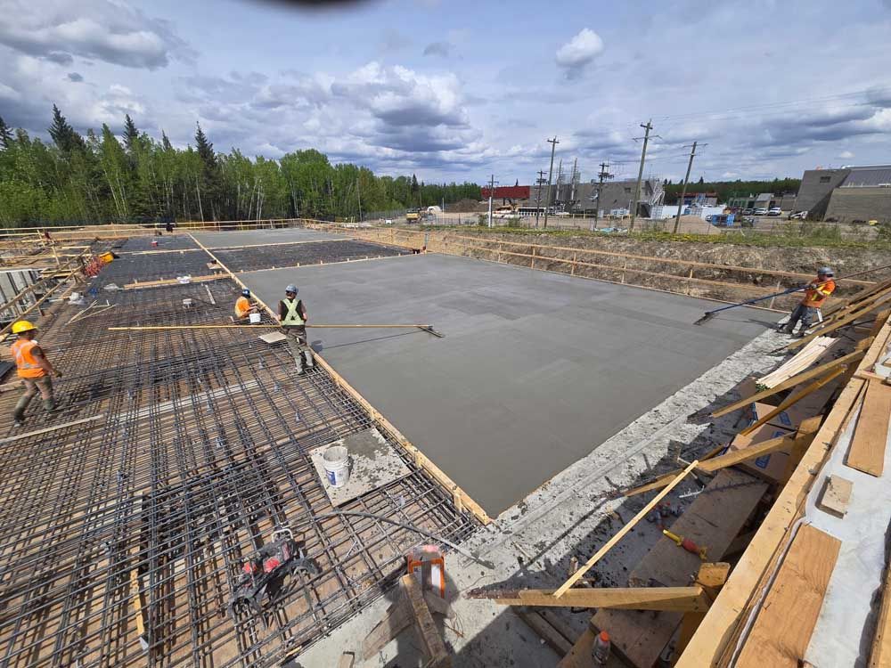 Construction workers pouring concrete over rebar at a large foundation site under a cloudy sky