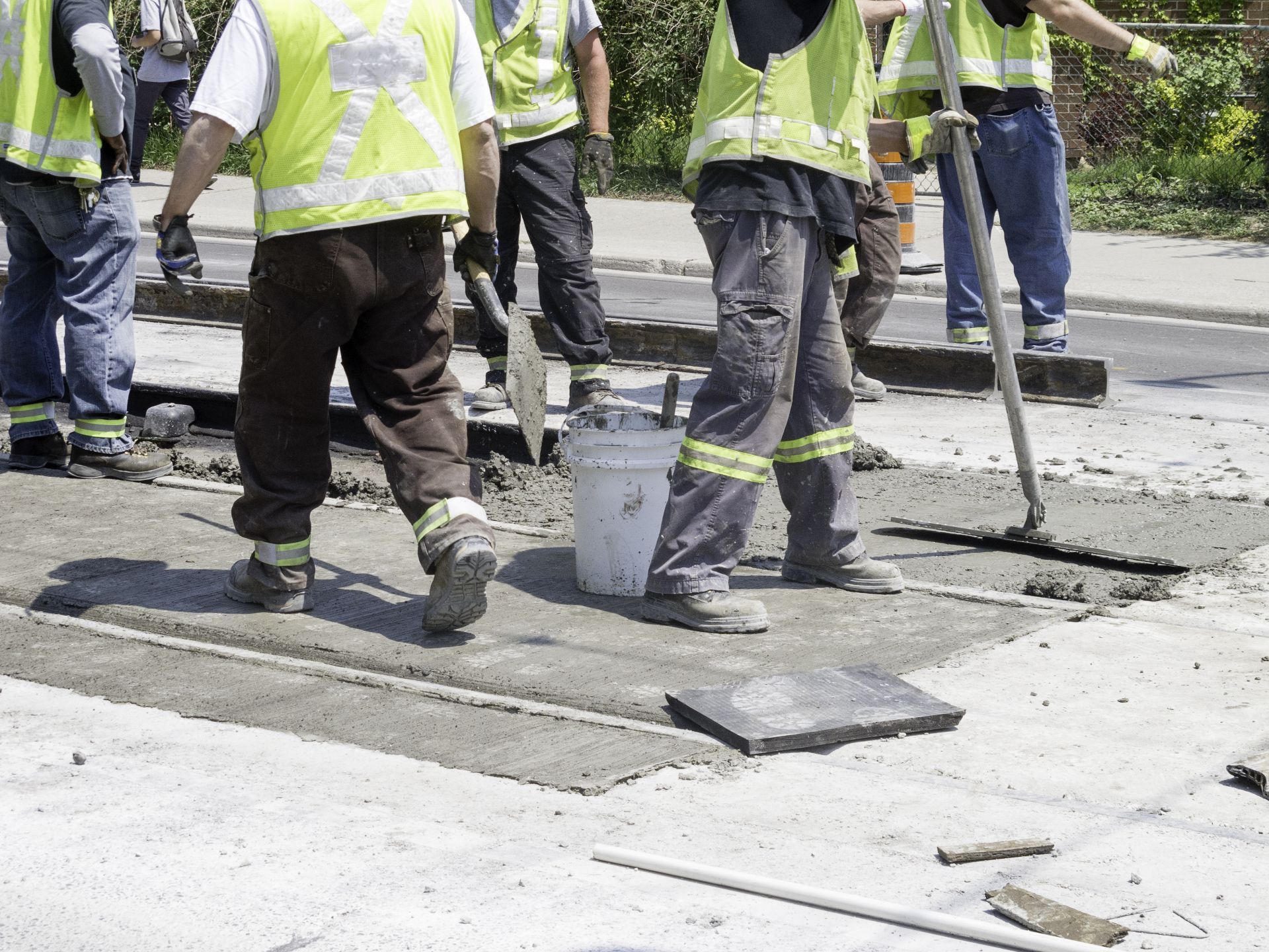 Construction workers in reflective vests pour and smooth concrete on a sidewalk repair site