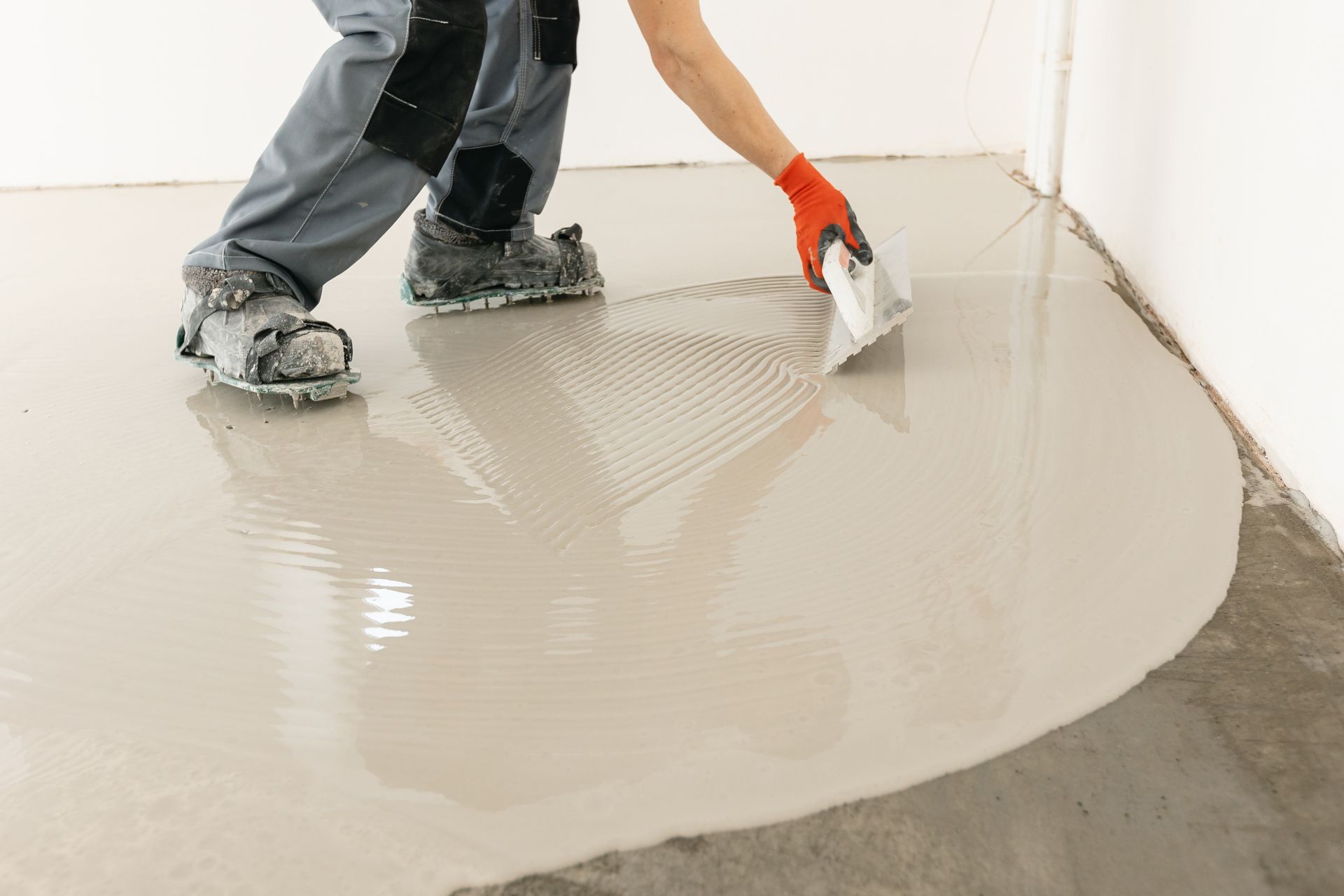 Worker spreading gray floor leveling compound with a trowel on a concrete floor