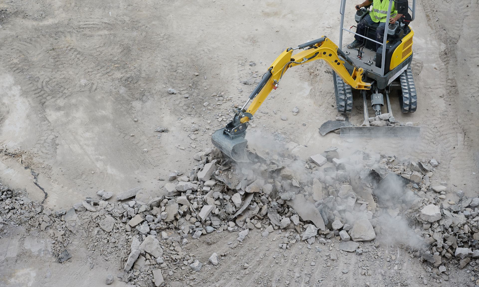 Yellow excavator arm digging rubble on a dusty construction site
