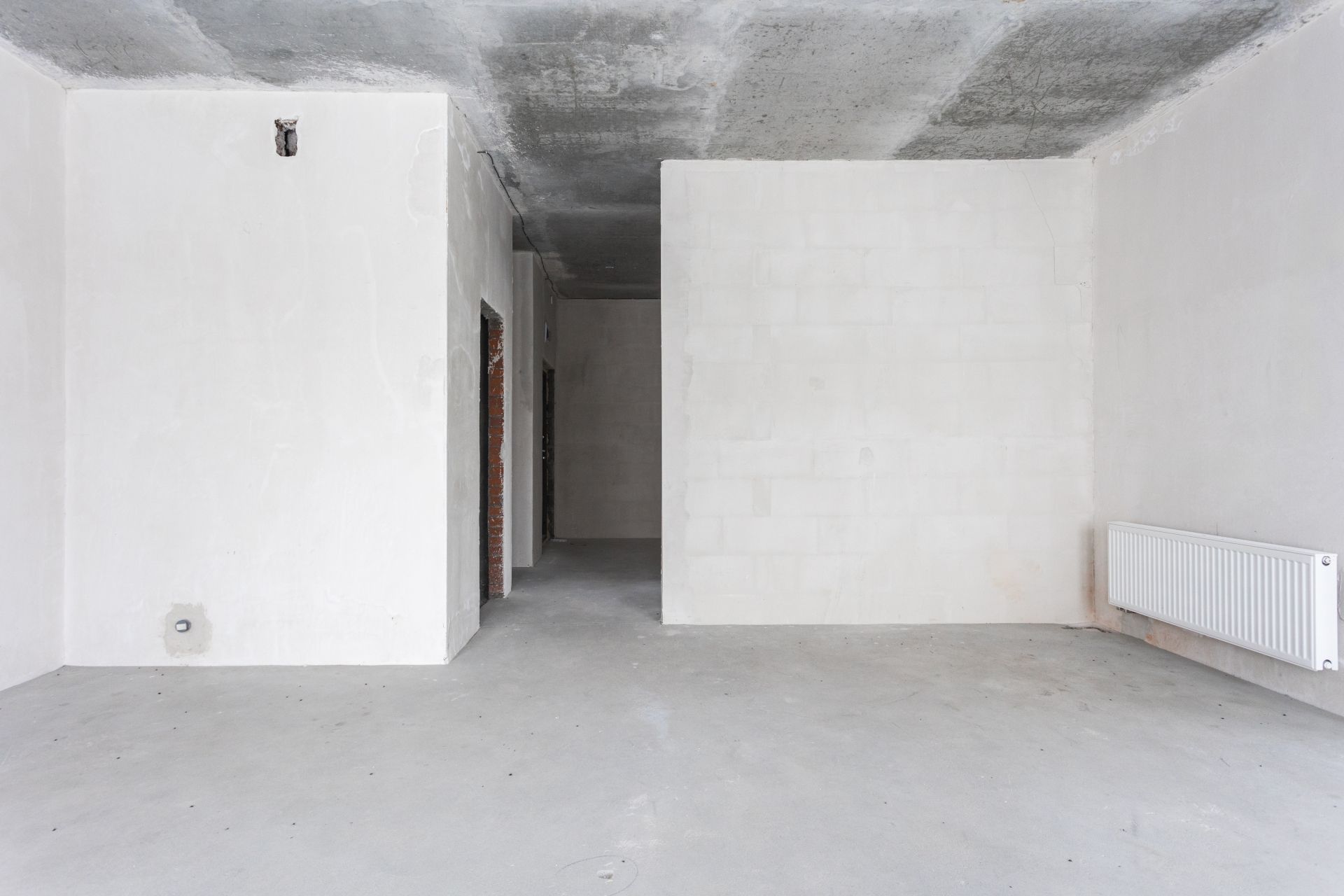 Empty unfinished room with white walls, concrete floor, exposed ceiling, and radiators along the right wall