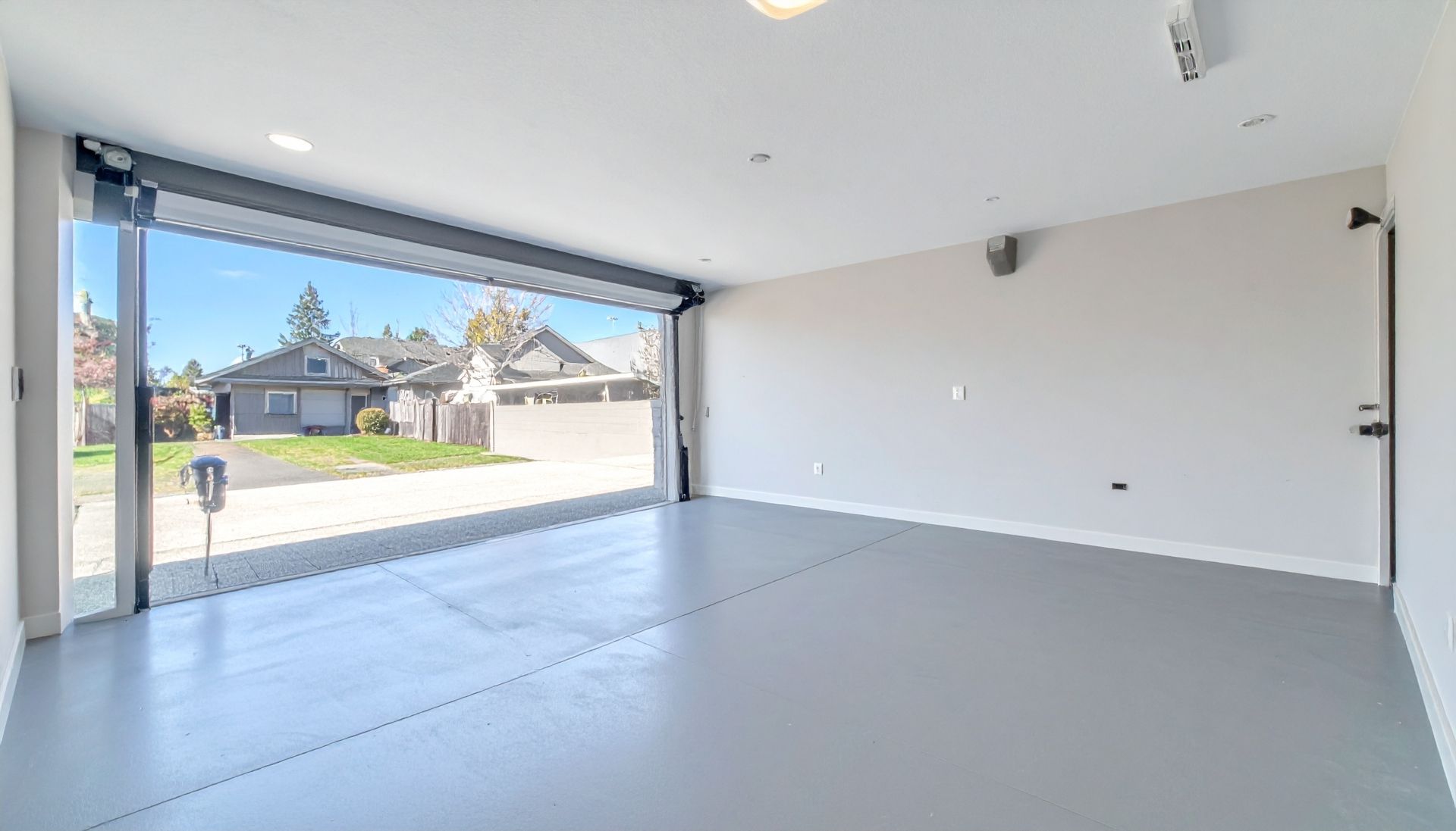 Bright empty modern room with large open garage-style door and view of a suburban street outside