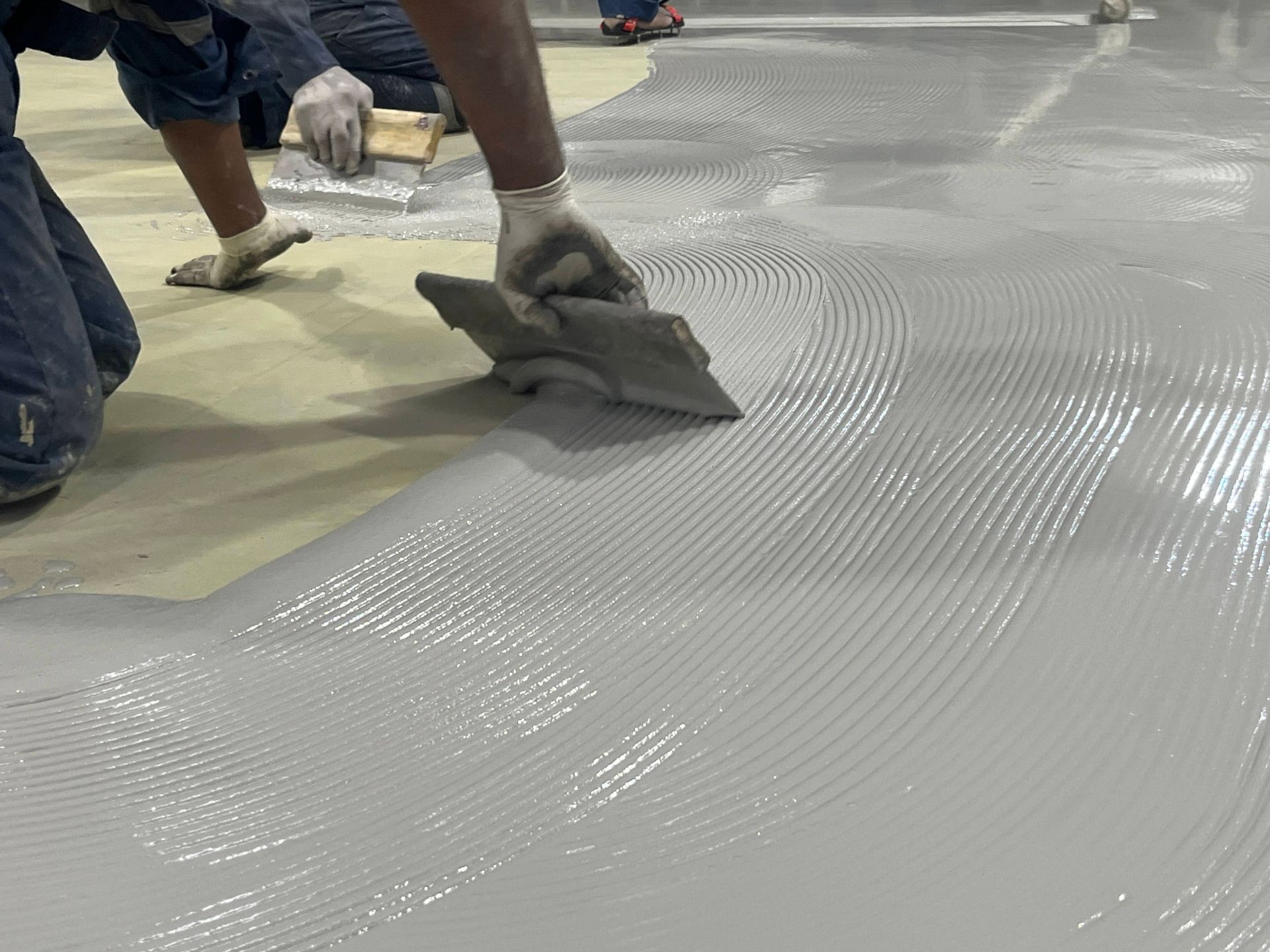 Workers smoothing wet concrete with trowels on a floor surface