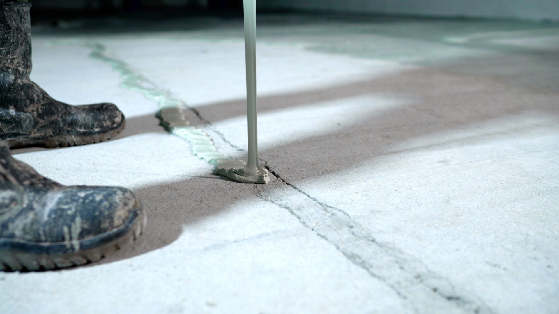 Mud-caked boots beside a vertical metal pole on a concrete floor