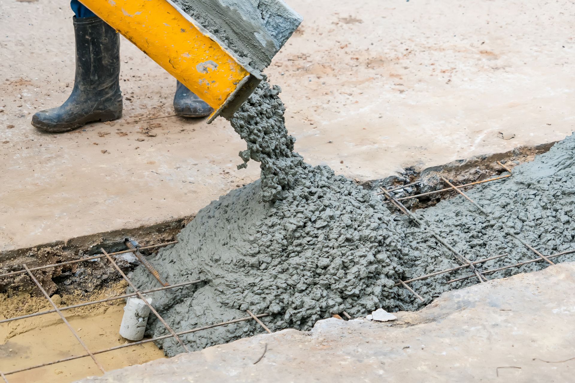 Concrete pouring from a yellow chute onto a trench at a construction site