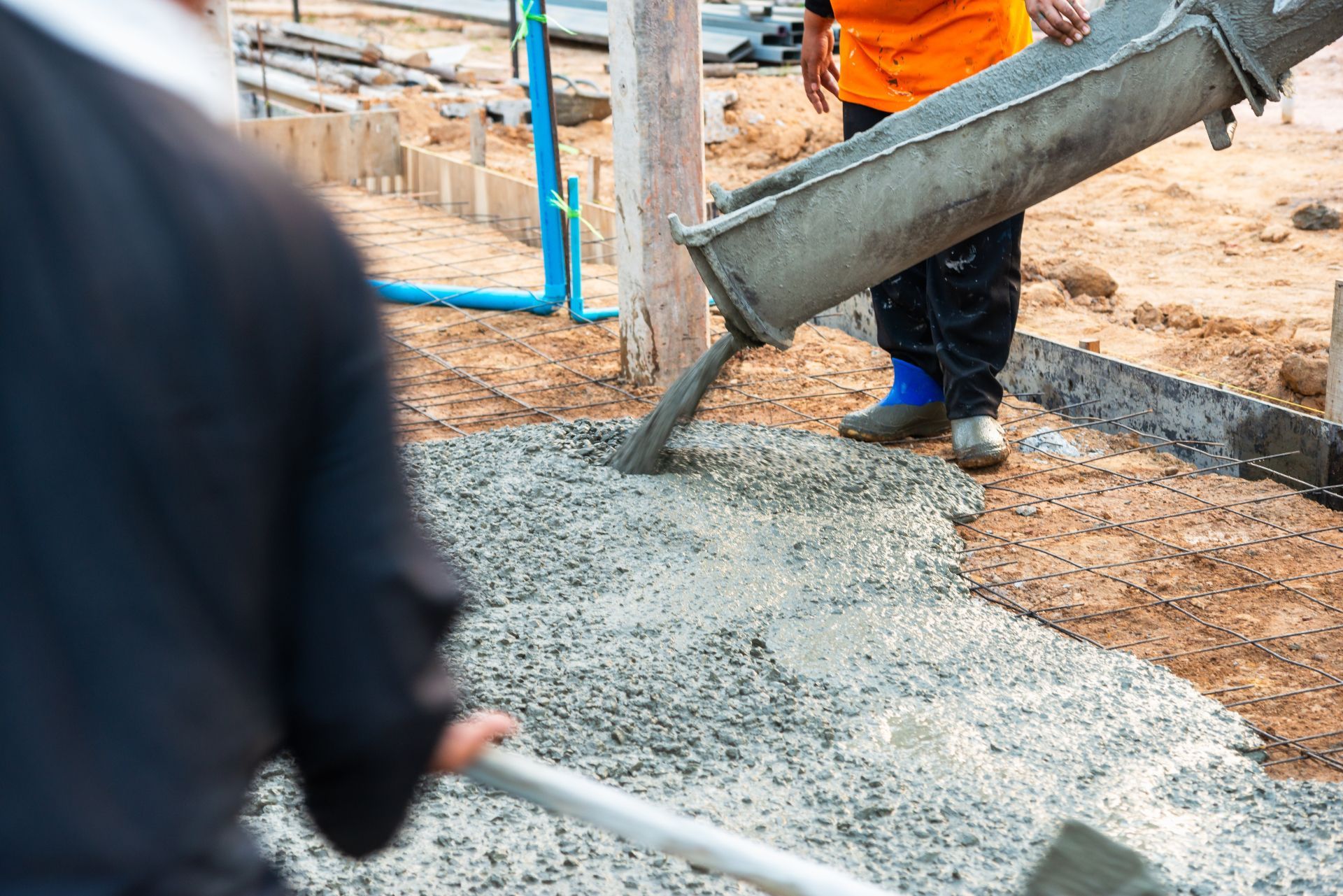 Workers pouring concrete into a foundation trench at a construction site