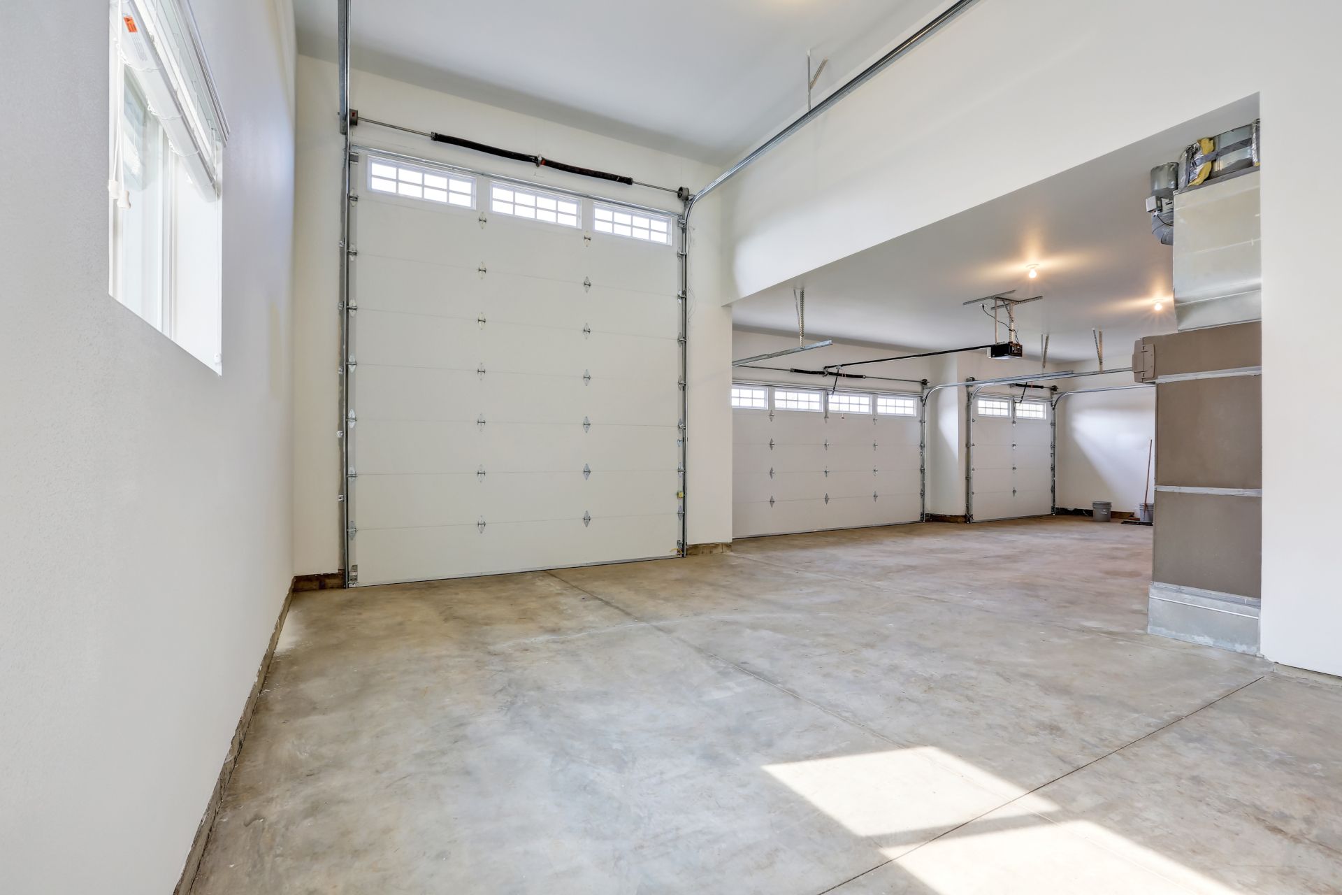 Empty white garage interior with concrete floor and closed overhead doors