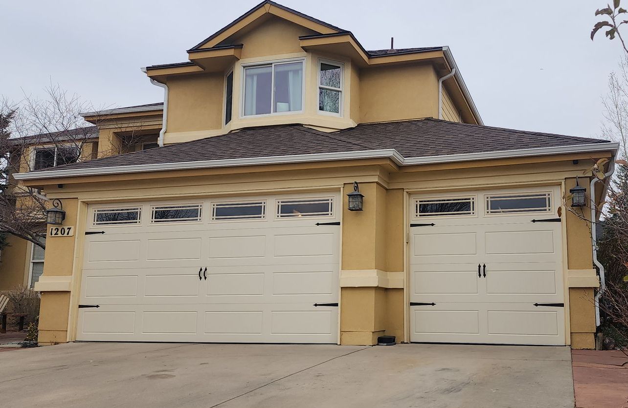 Two-story beige house with tiled roof and two white garage doors.