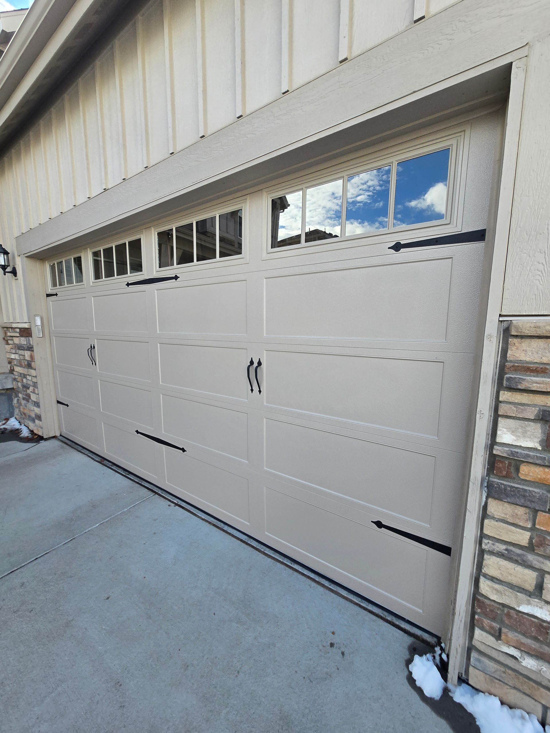 Light gray garage door with windows in a driveway beside stone and metal siding