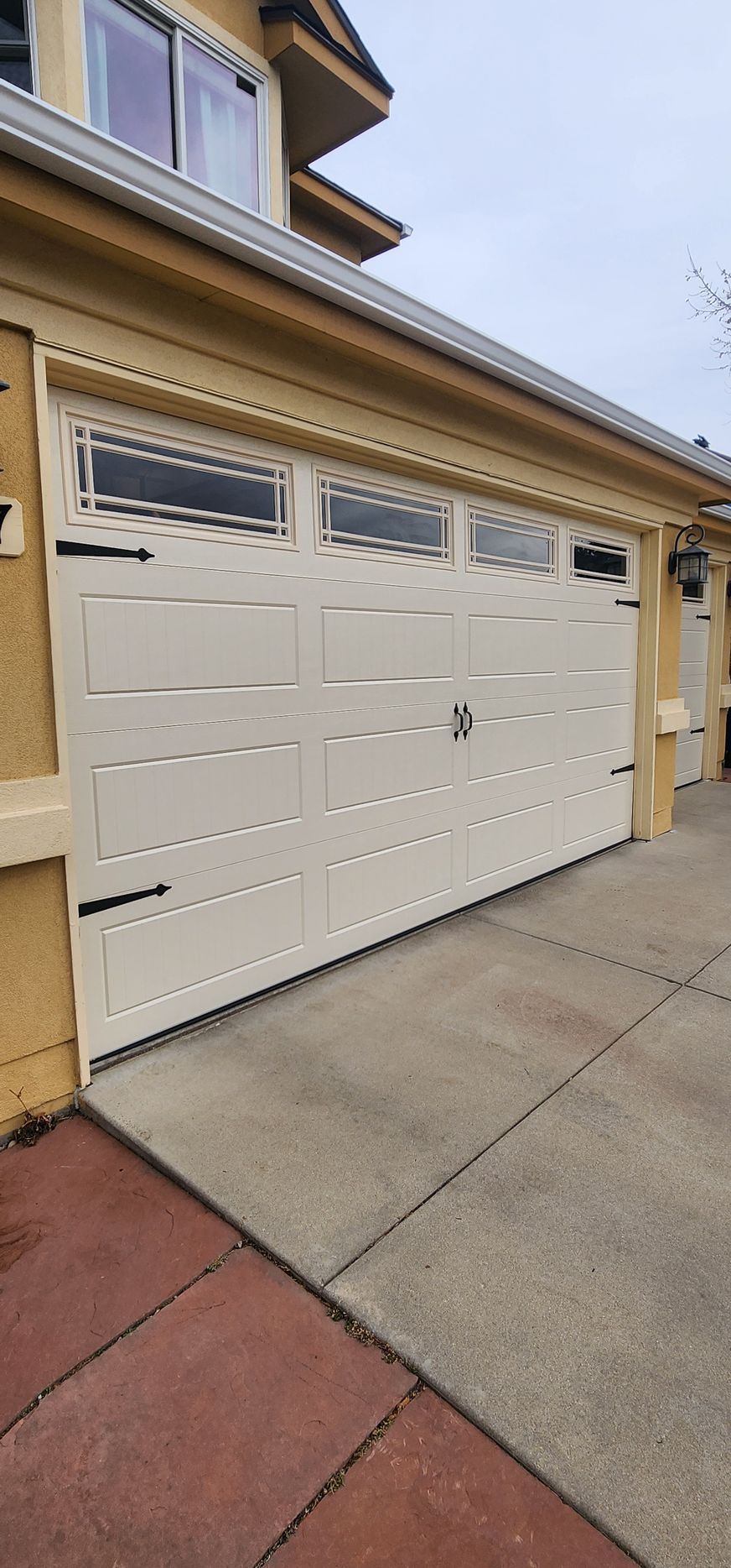White garage door with narrow windows on a beige house exterior beside a concrete driveway