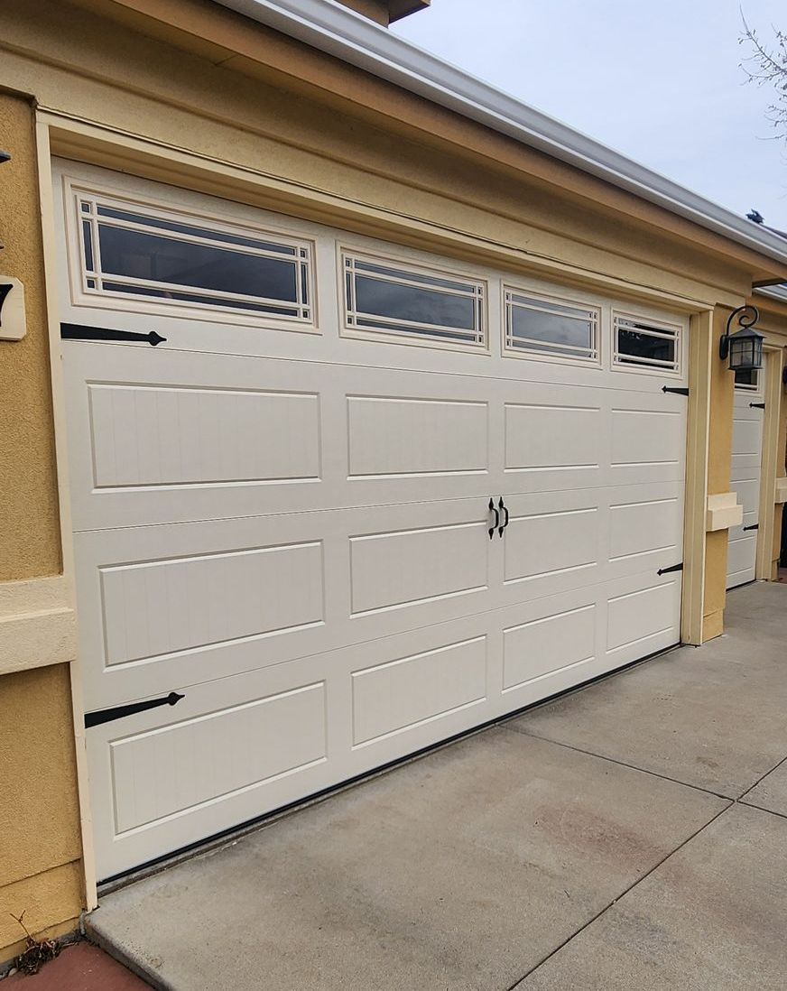 White double garage door with small windows on a beige house exterior, viewed from the driveway