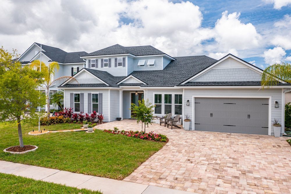Modern two-story suburban house with white trim, gray roof, stone driveway, and landscaped front yard