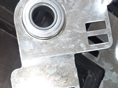 Close-up of a metal bracket with a circular bearing and rectangular cutouts on a dark surface