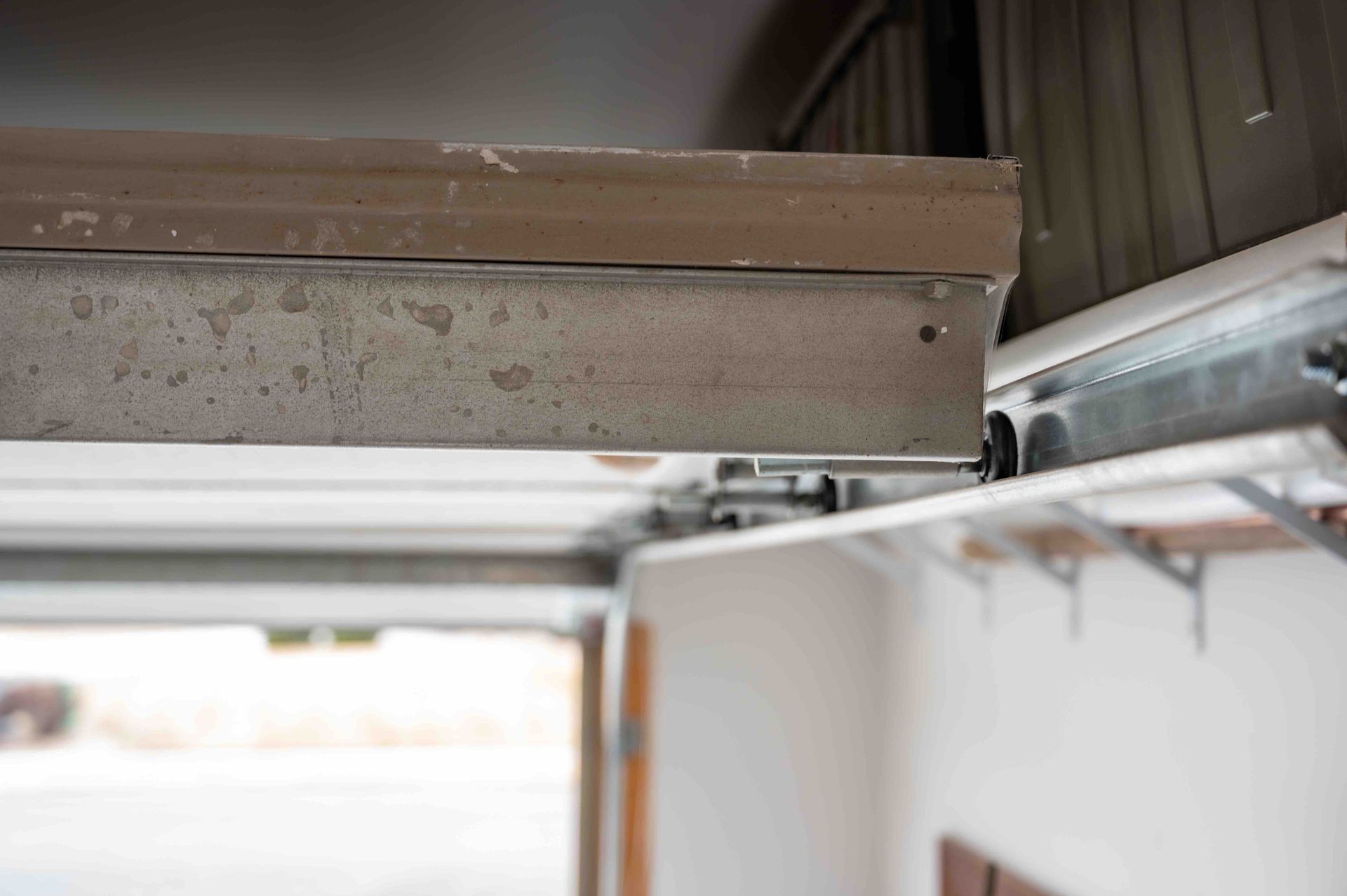 Close-up of a garage door track and overhead spring mechanism with brown metal paneling.