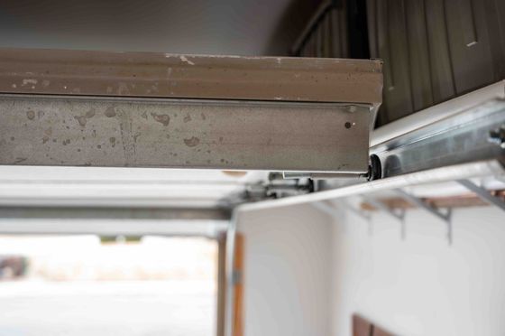 Close-up of a garage door track and roller mechanism with dust and brown metal parts.