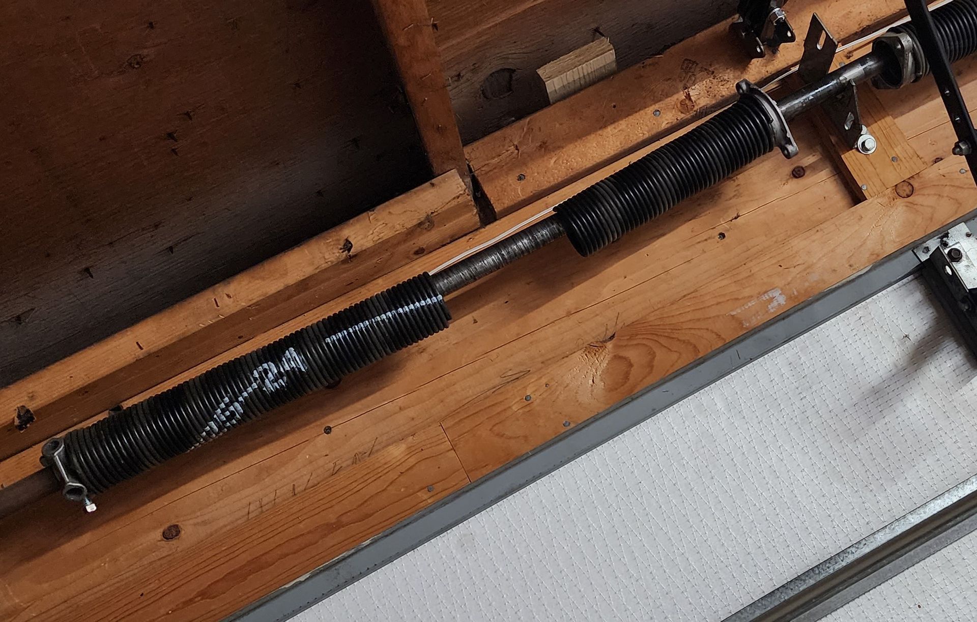 Black metal spring mechanism on a wooden surface beside a gray panel