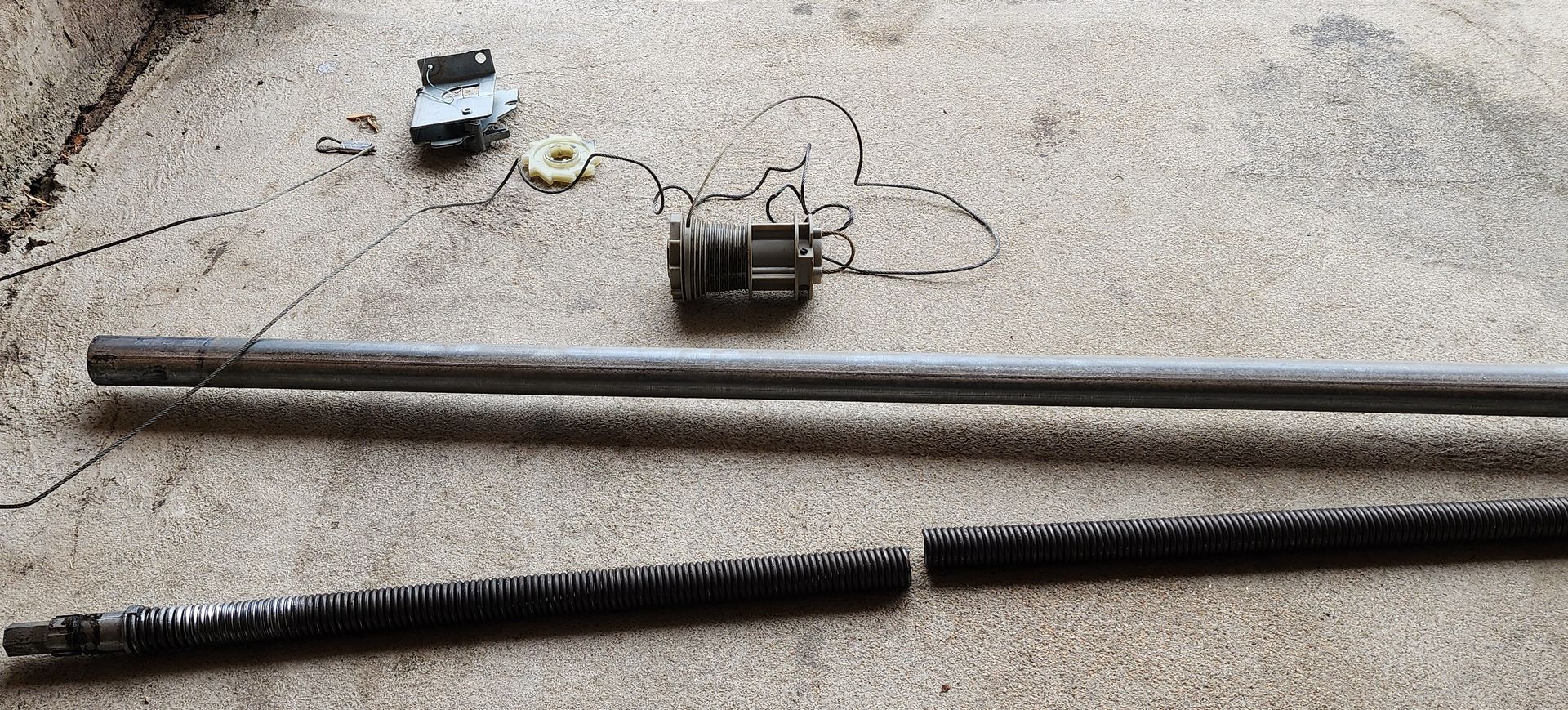 Scattered tools and metal rods on concrete, including a small motor and a black cord.