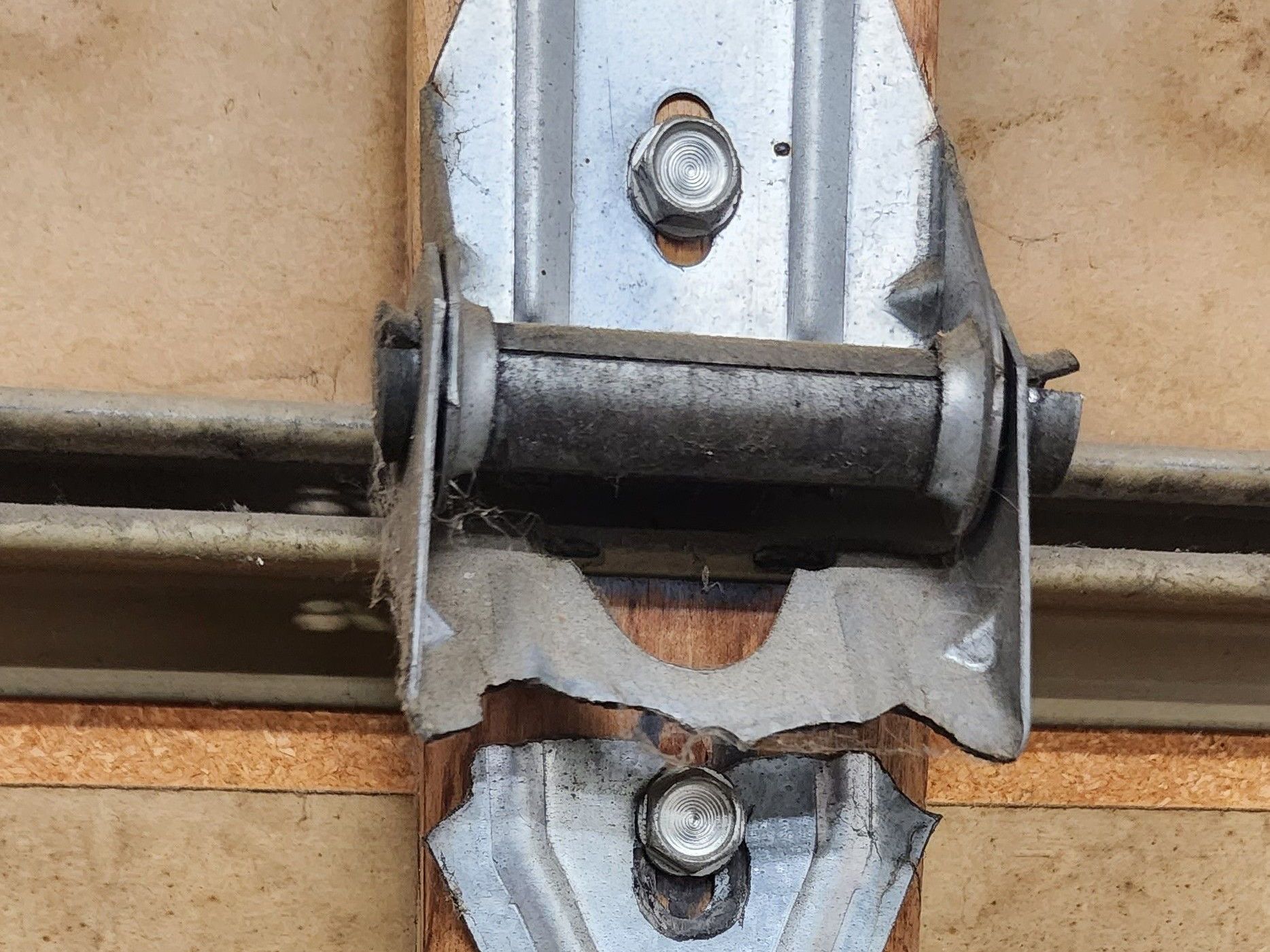 Broken metal hinge mounted on a tan door or panel, with visible screws and bent bracket.