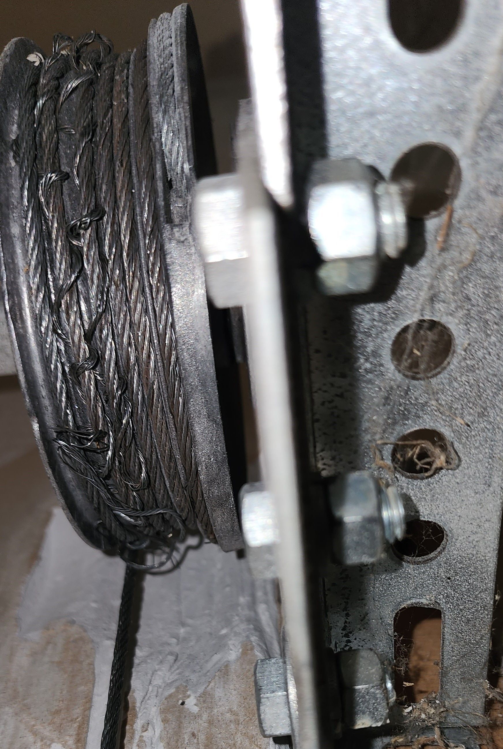 Close-up of a worn black pulley wheel and metal bracket with bolts and a white spacer.