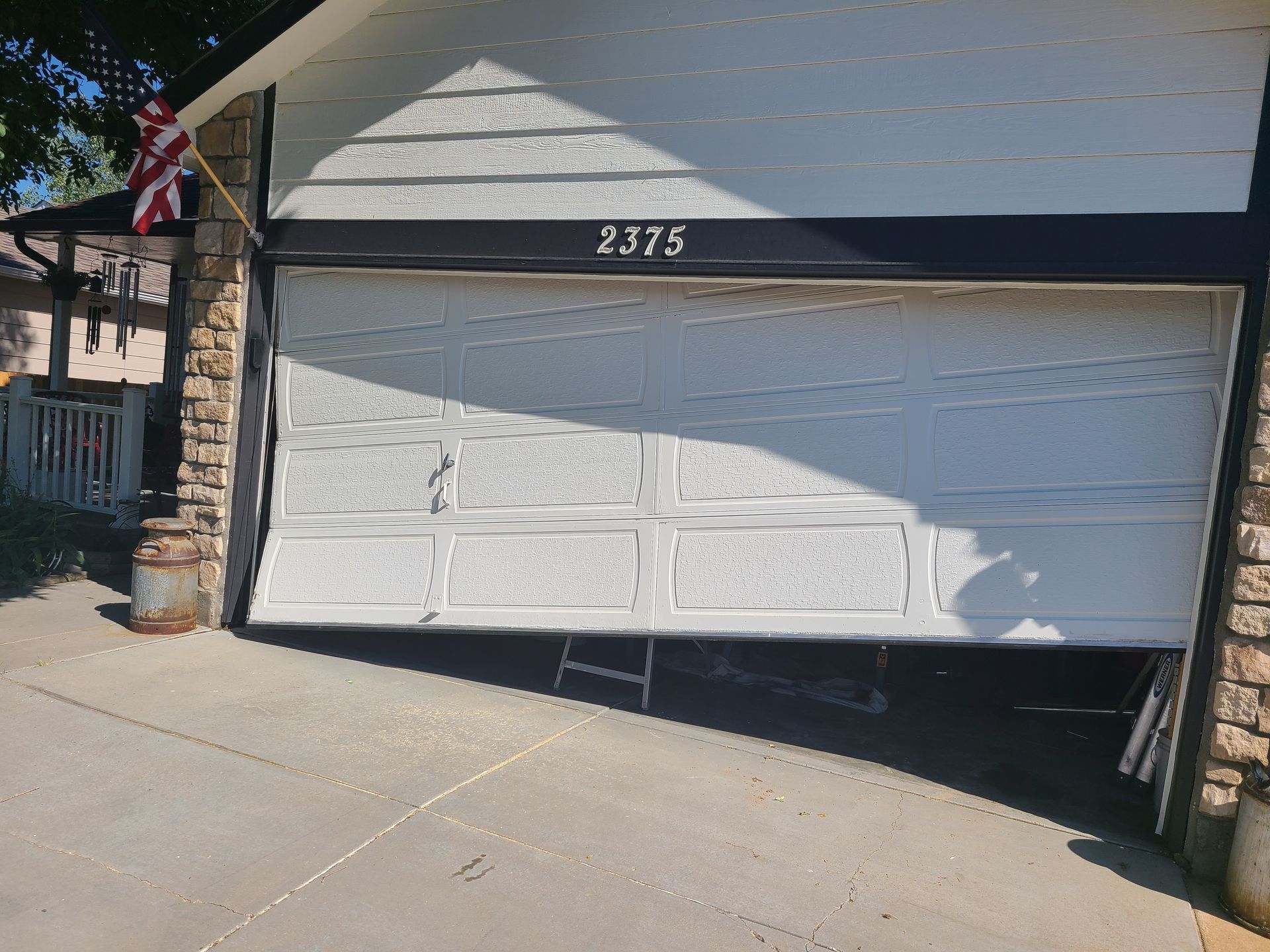 White garage door beneath house number 2375, partially open with a ladder visible inside.