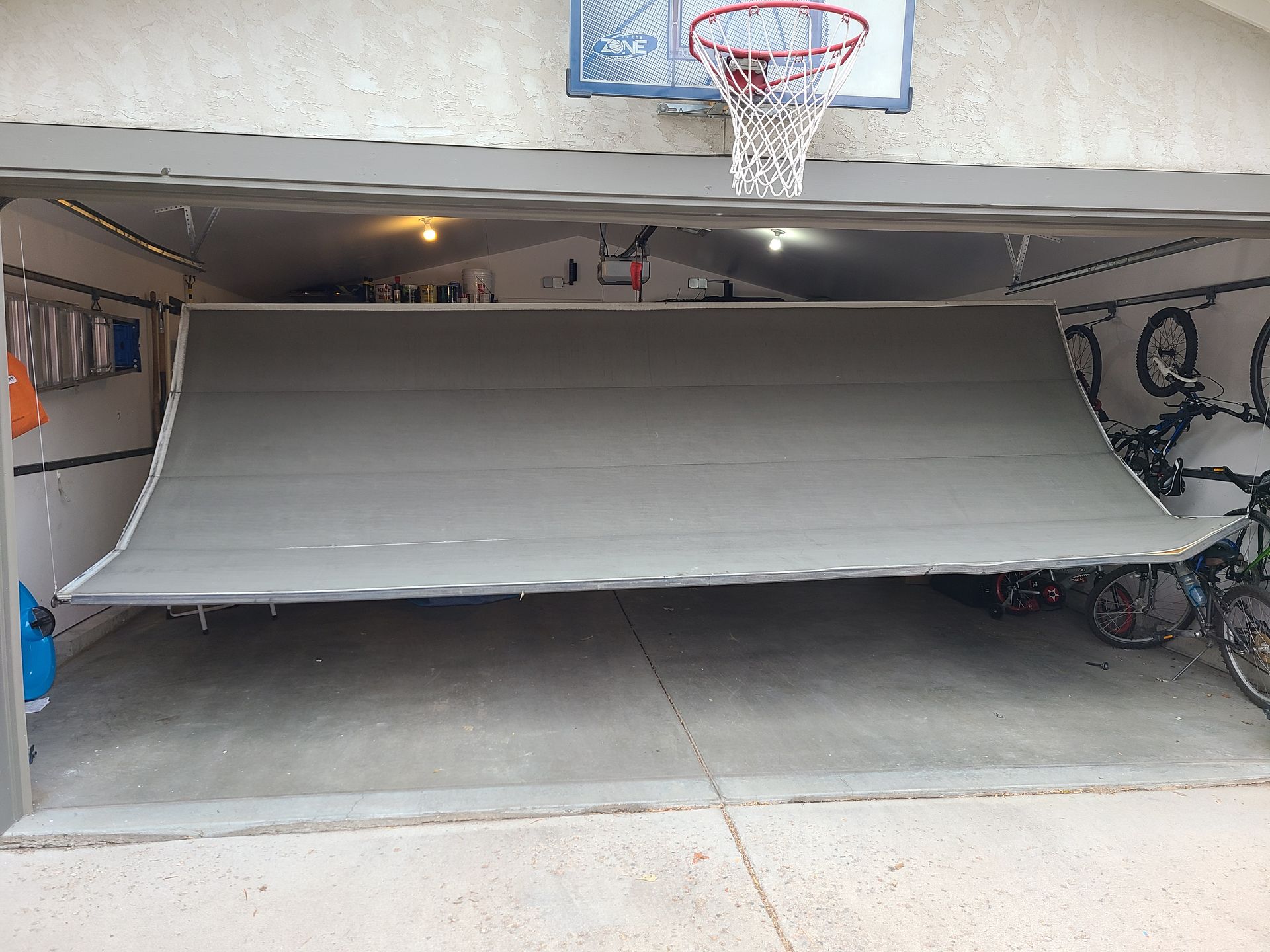 Garage doorway covered by a large gray tarp or screen beneath a basketball hoop