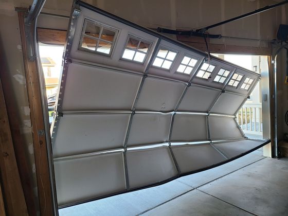 Large segmented metal garage door partially open inside an industrial doorway.