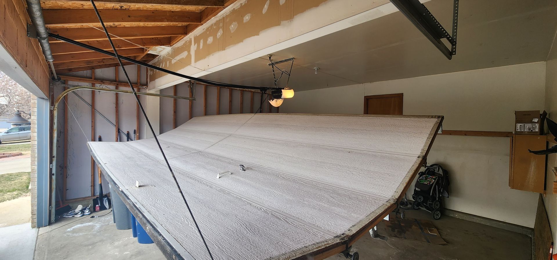 Large white folding garage door panel leaning inside a cluttered garage under construction