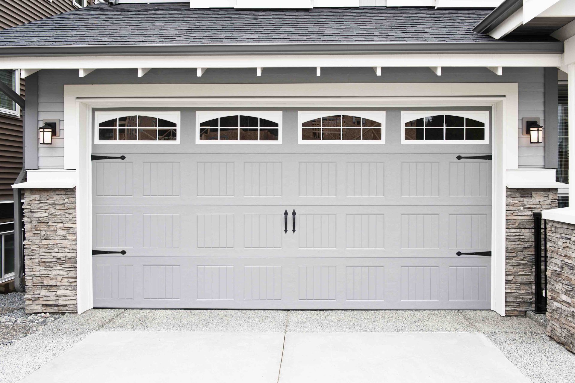 Front view of a white double garage door with arched windows and stone-trimmed pillars