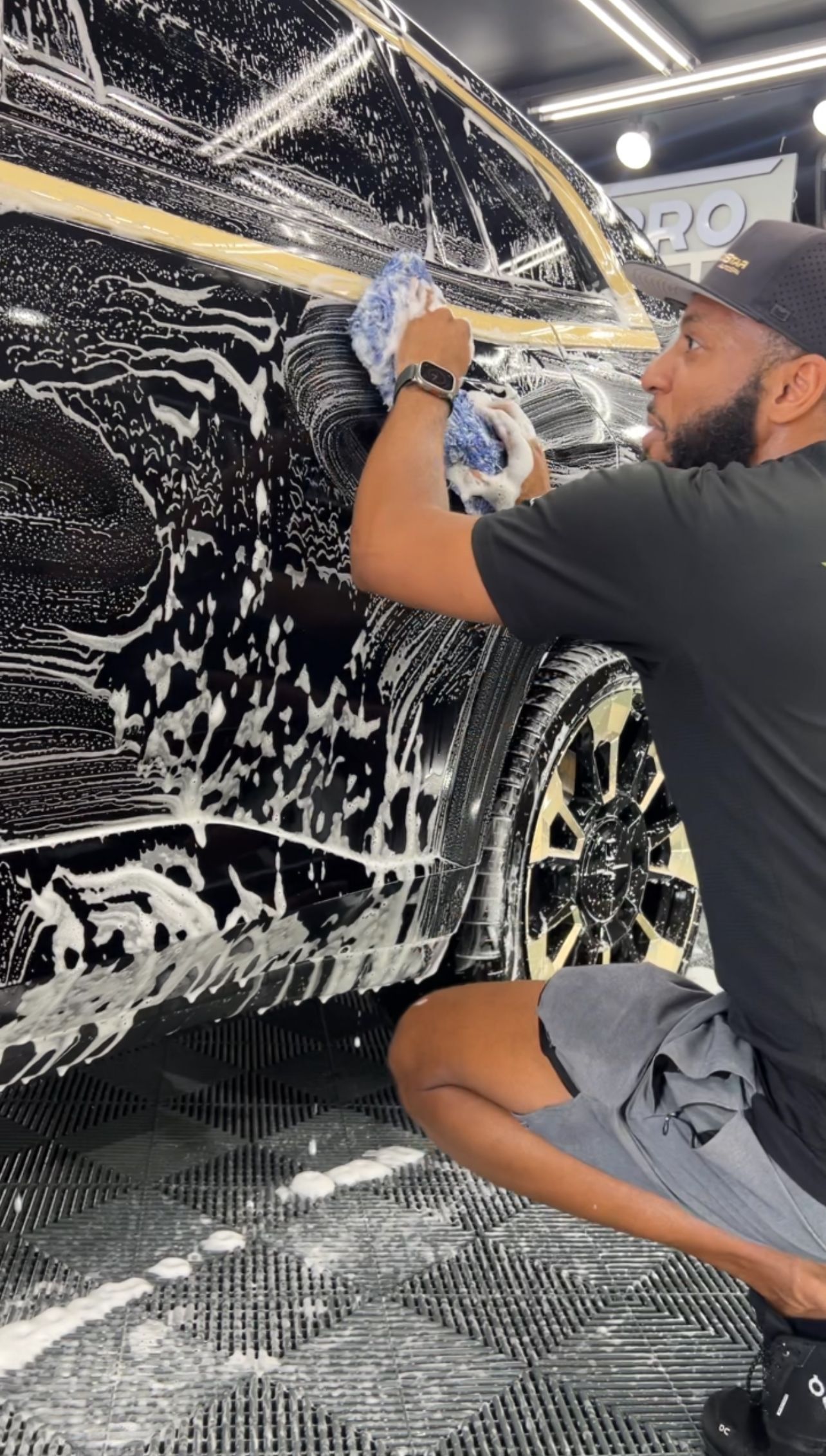 A man is kneeling down to wash a car in a garage.