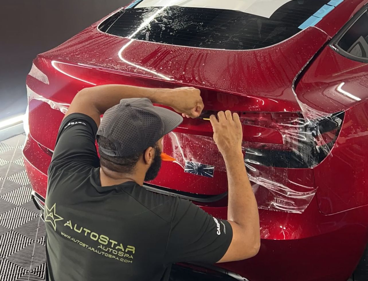 A man is wrapping a red car with plastic wrap.