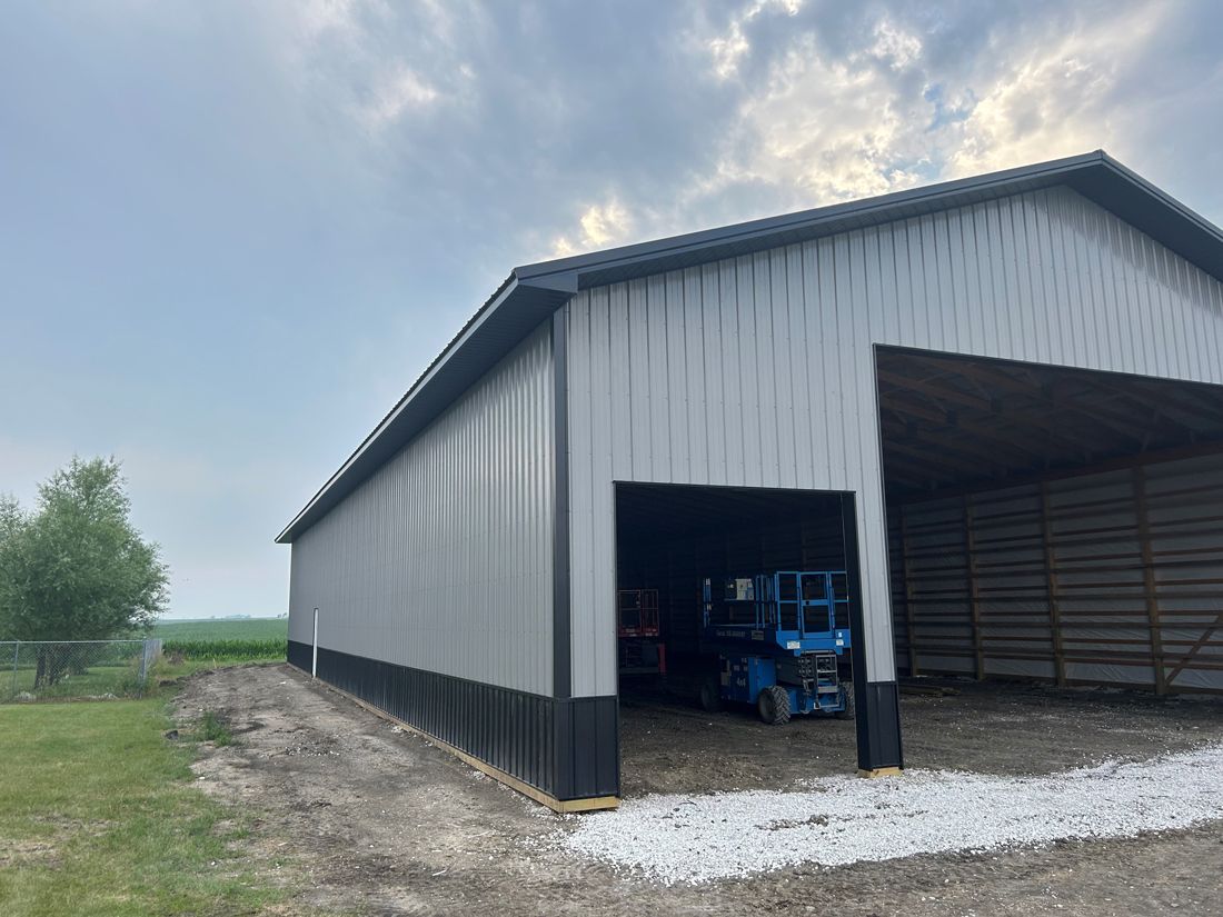 Large metal-sided agricultural building with open front and blue lift inside, gray and black accents.