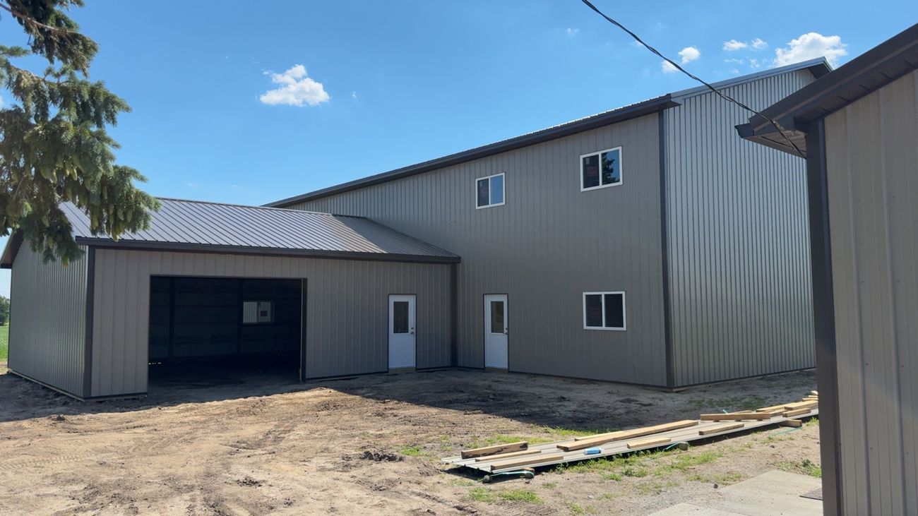 A two-story gray metal building with garage and white doors and windows under a bright blue sky.