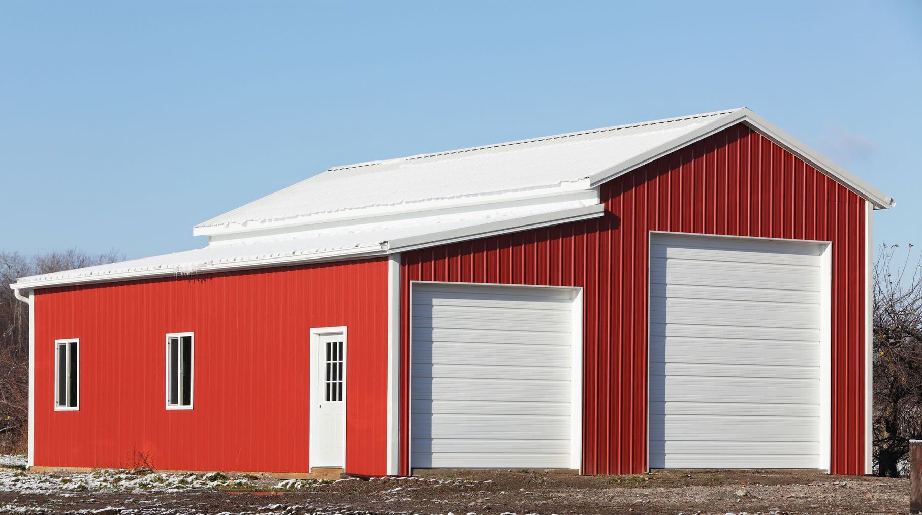 Red barn with a white roof and garage doors, set against a blue sky.