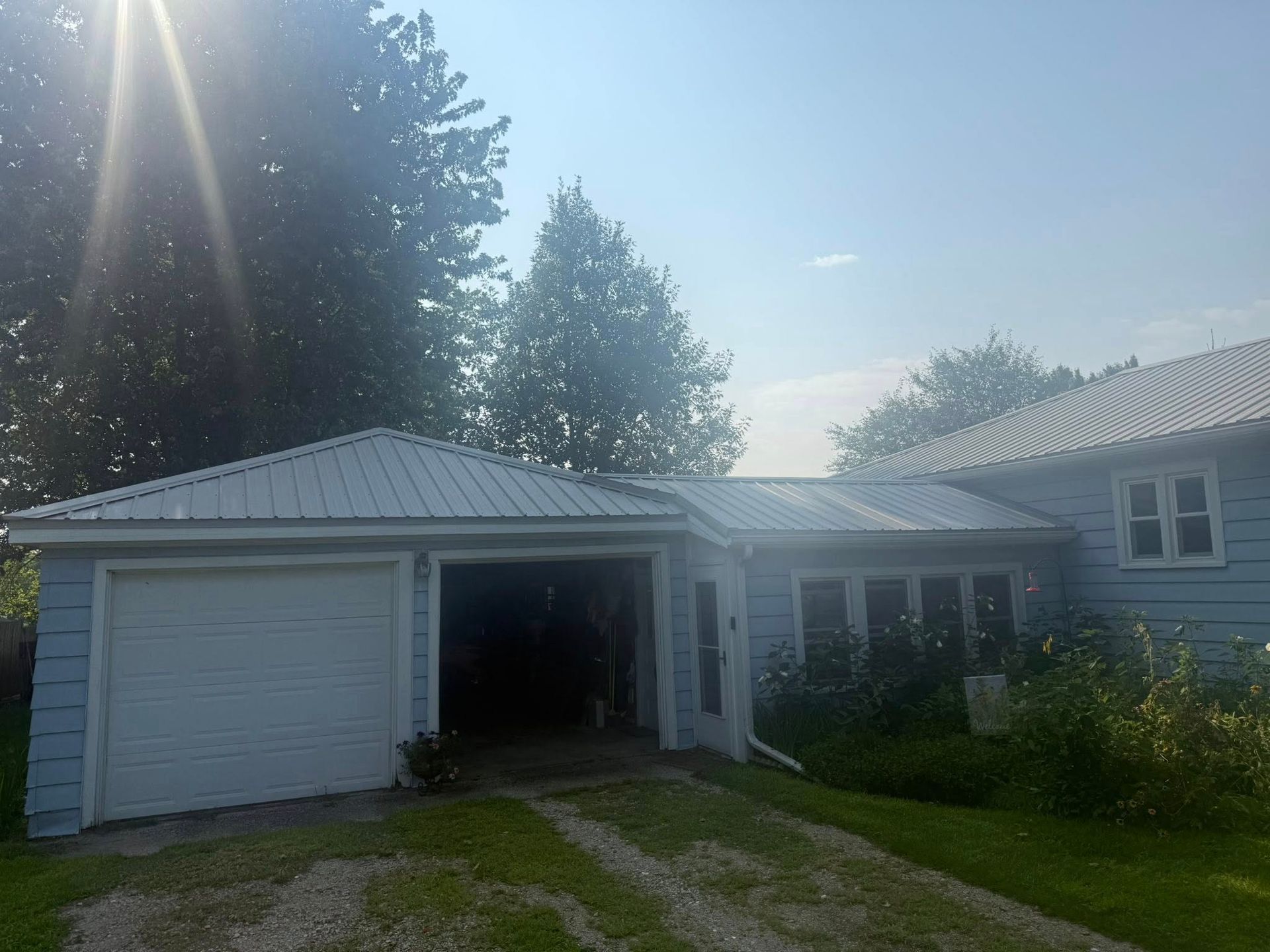 Light blue house with a white garage door and metal roof on a sunny day.