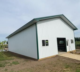 White barn with green trim, open doorway, windows, set on a grassy area under a cloudy sky.