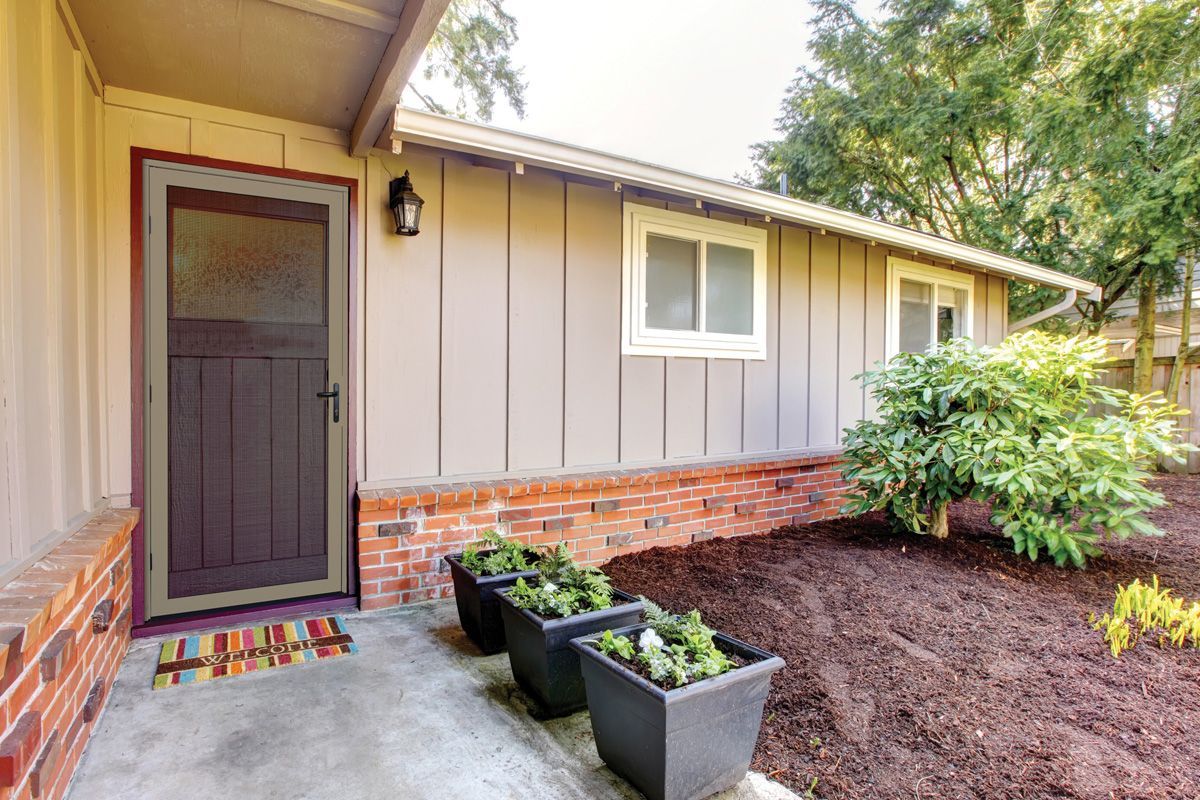 Side of a home with a screen door, windows, and garden planters along the walkway