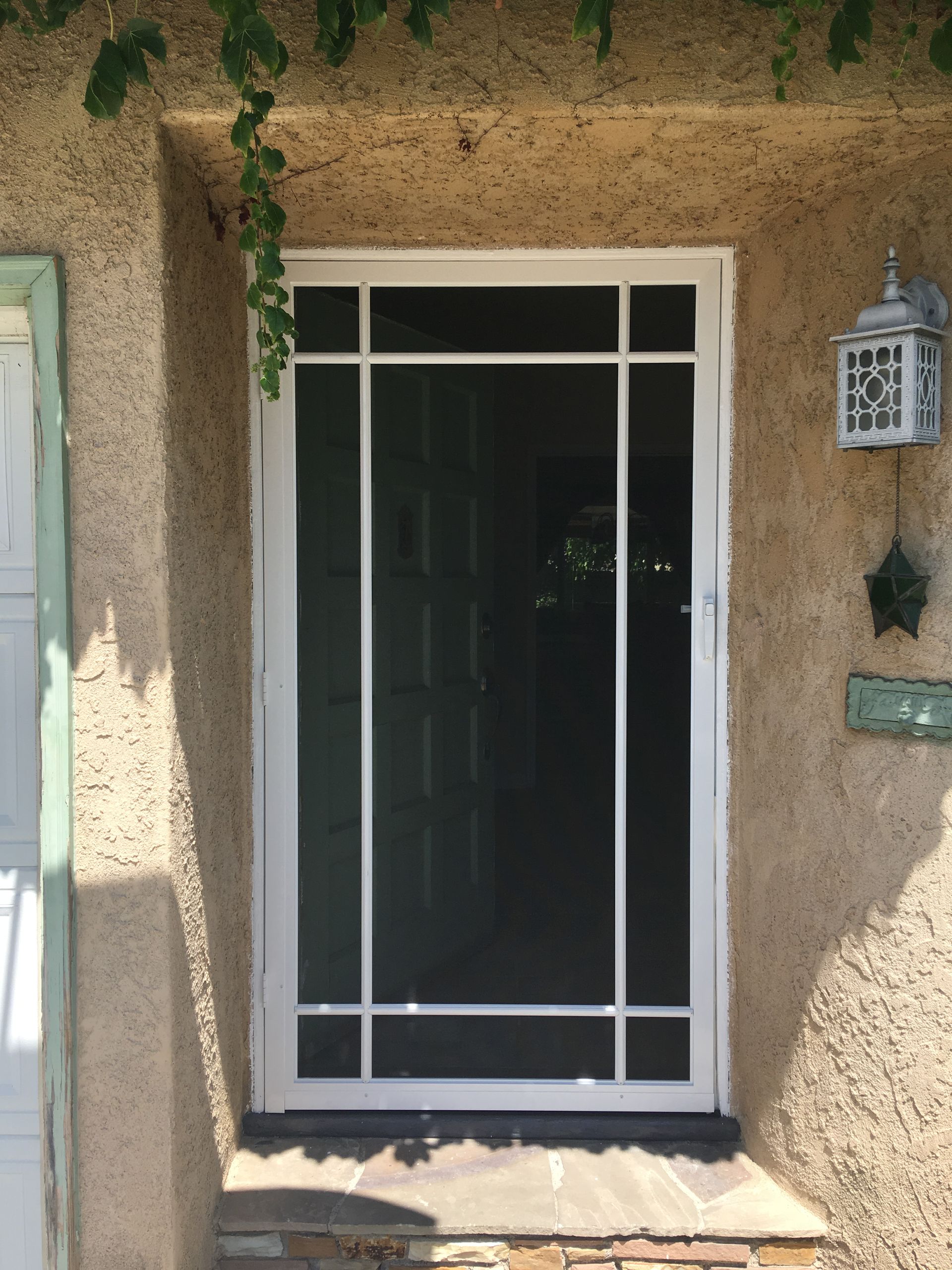 Front entry door with a white security screen door and surrounding stucco wall