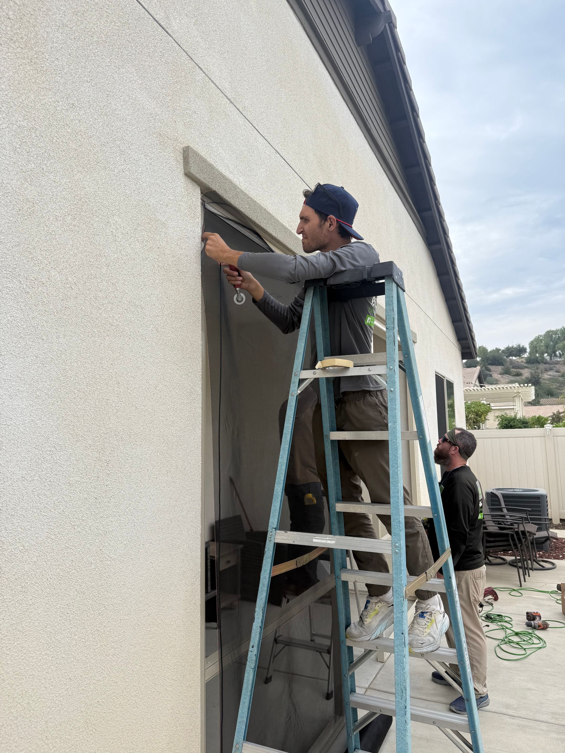 Technician on a ladder installing a window screen on a home exterior