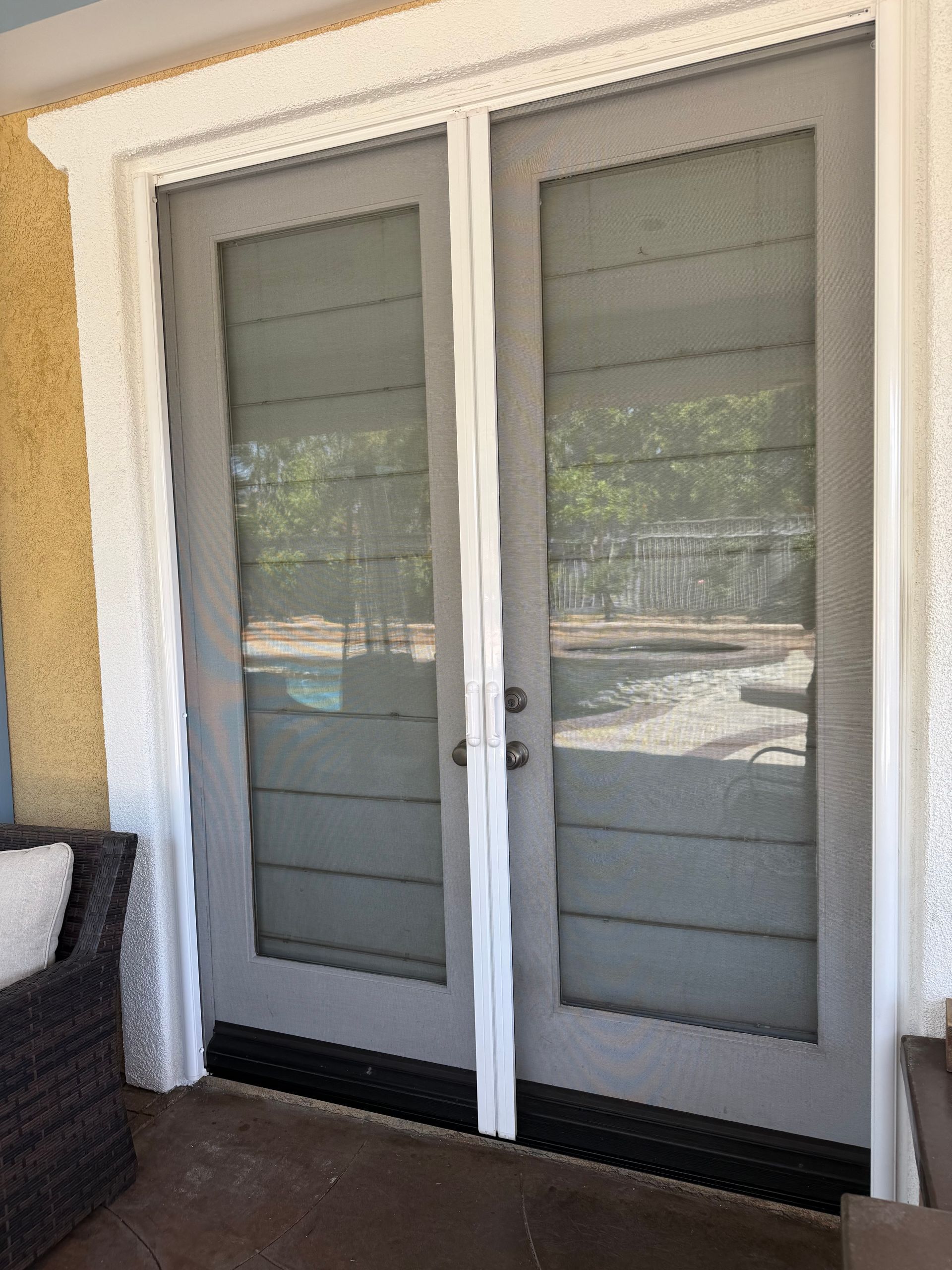 White double retractable screen door installed and solid double doors showing through screen.
