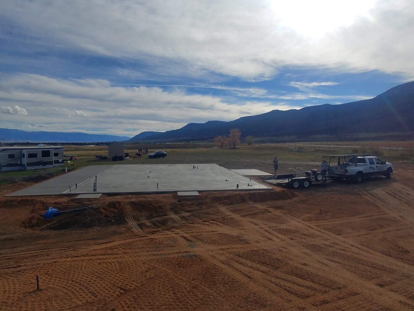 A truck is parked in a dirt field next to a concrete slab.