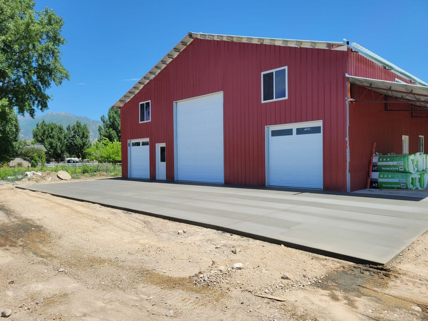 A red barn with white garage doors and a concrete driveway in front of it.