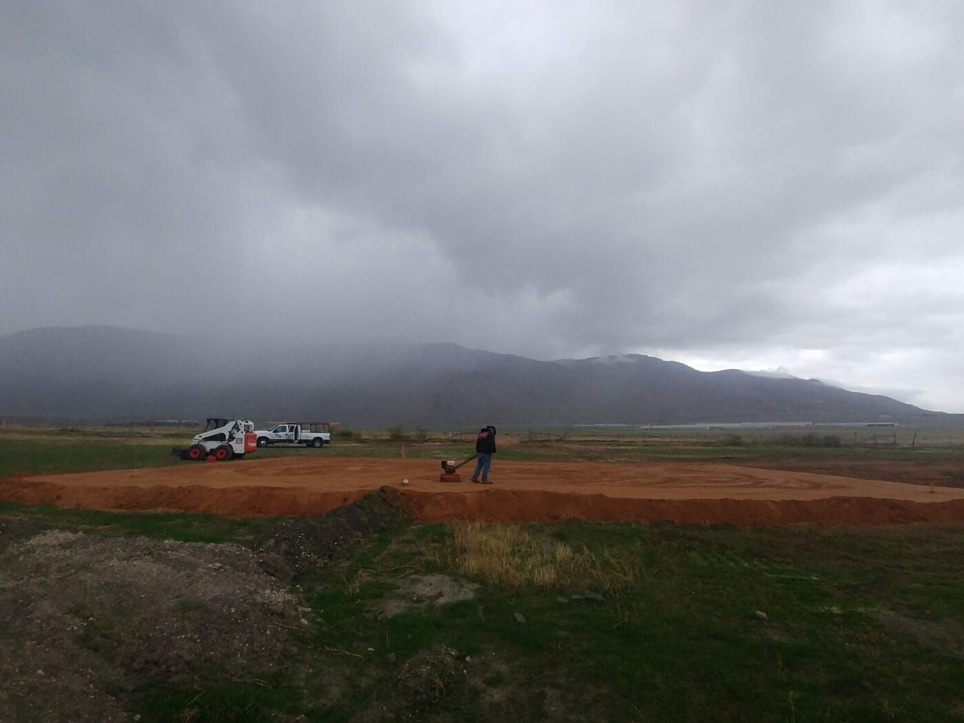 A man is walking a dog in a field with mountains in the background.