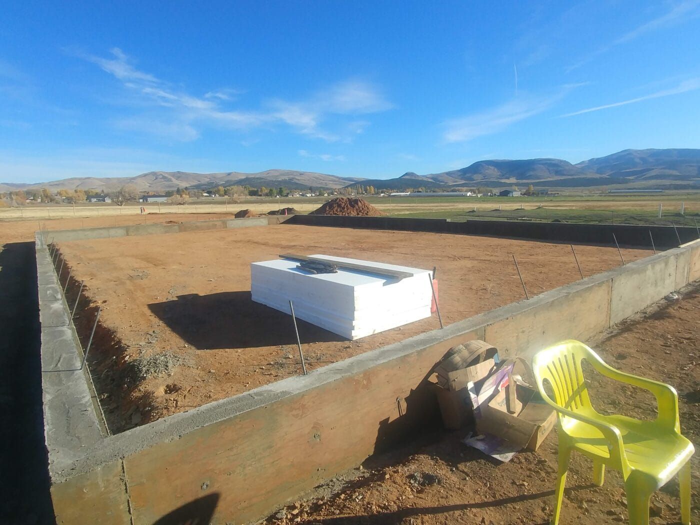 A yellow chair is sitting in the dirt next to a concrete wall.