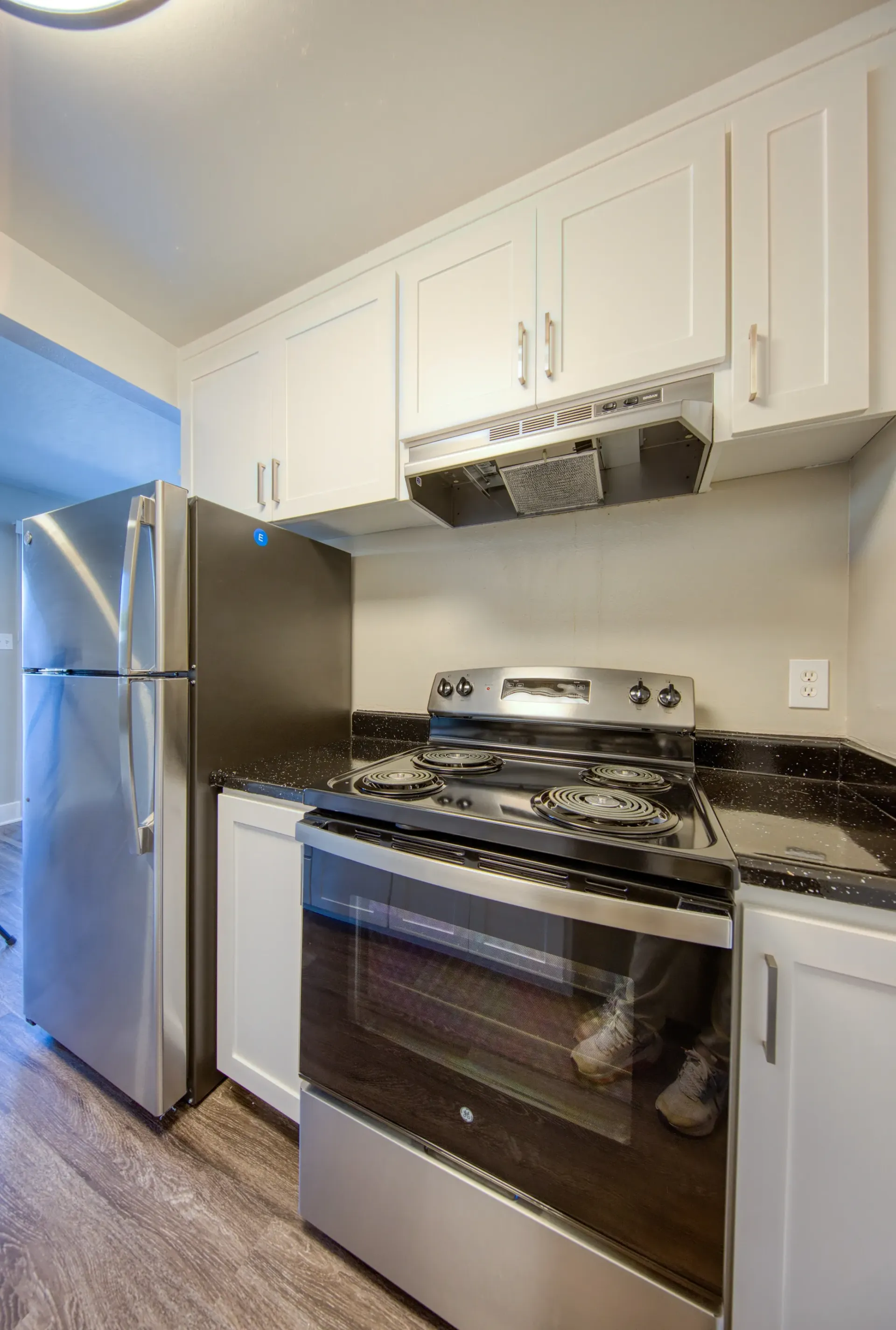 Modern kitchen with stainless steel refrigerator and oven, white cabinets, and granite countertops.