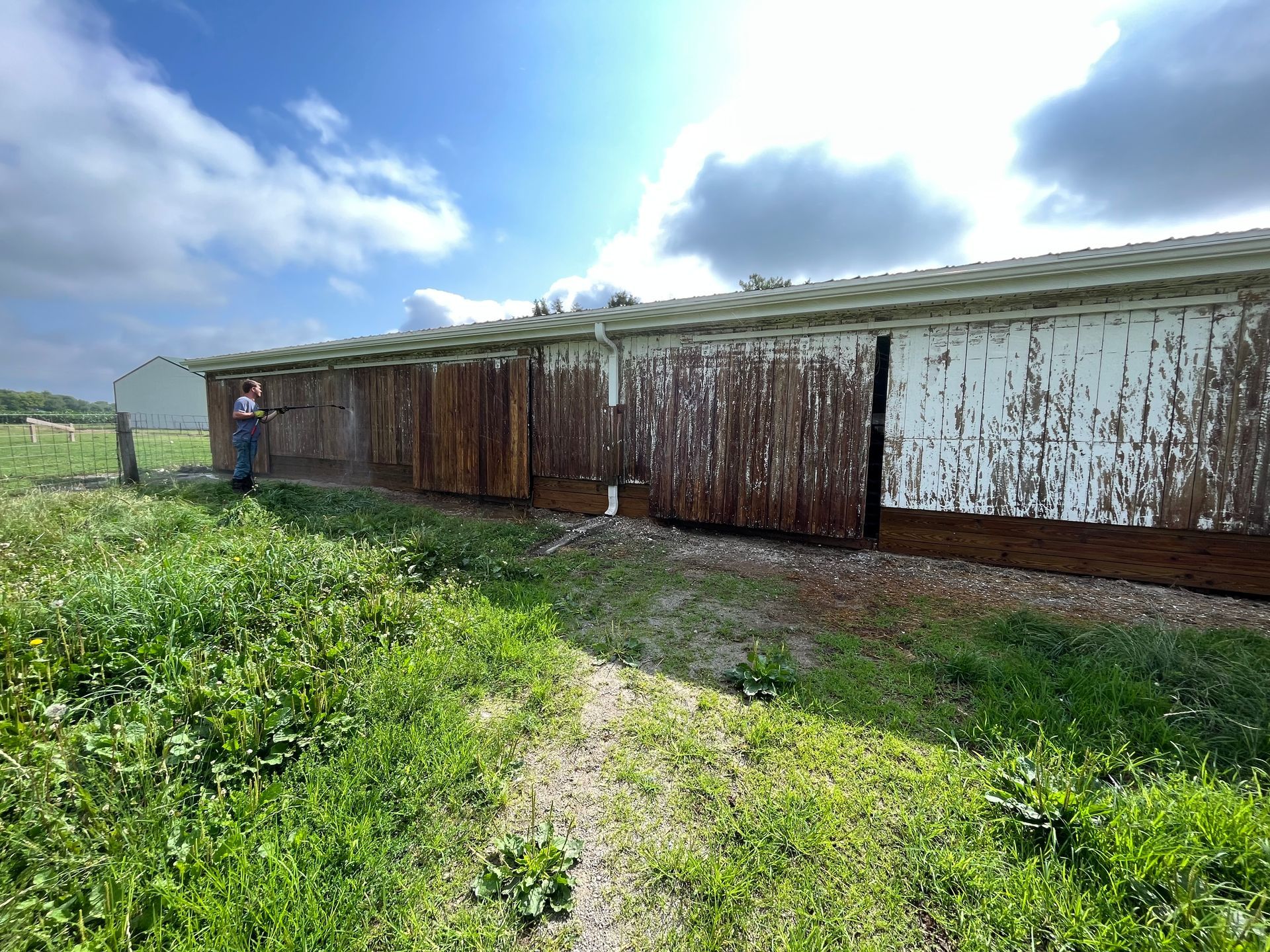 A man is standing in front of a rusty building in a field.