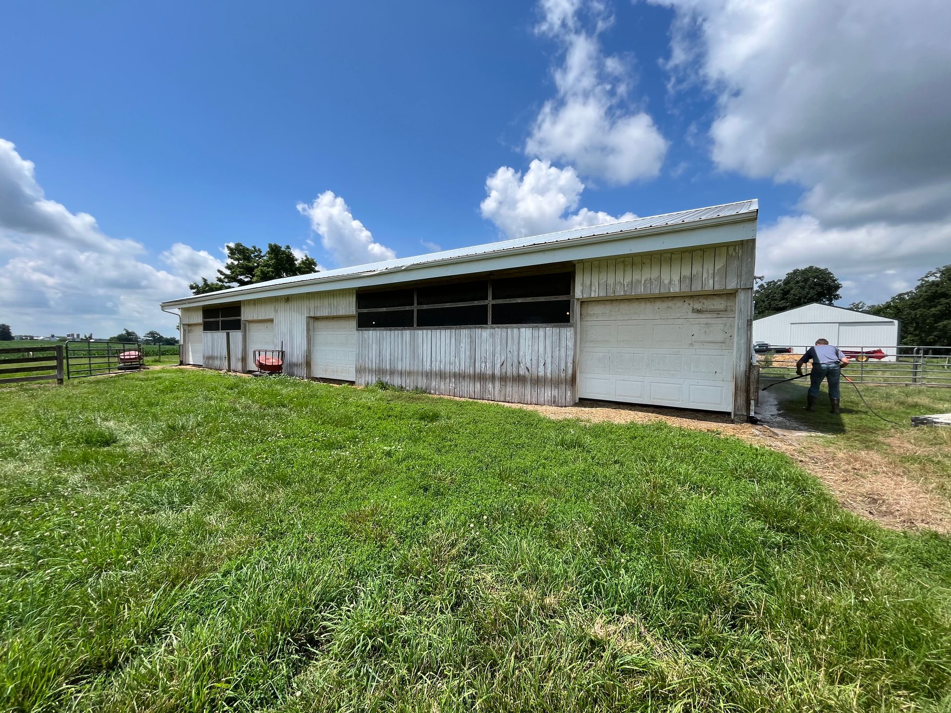 A white barn is sitting in the middle of a grassy field.