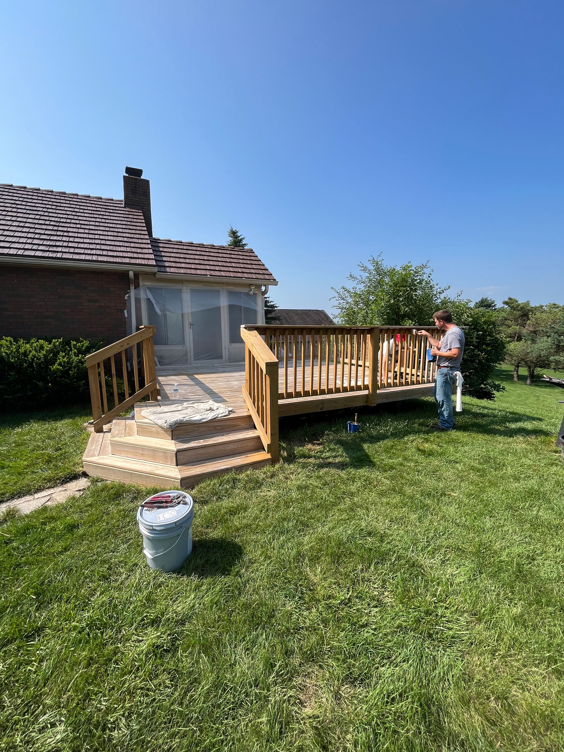 A man is painting a wooden deck in front of a house.