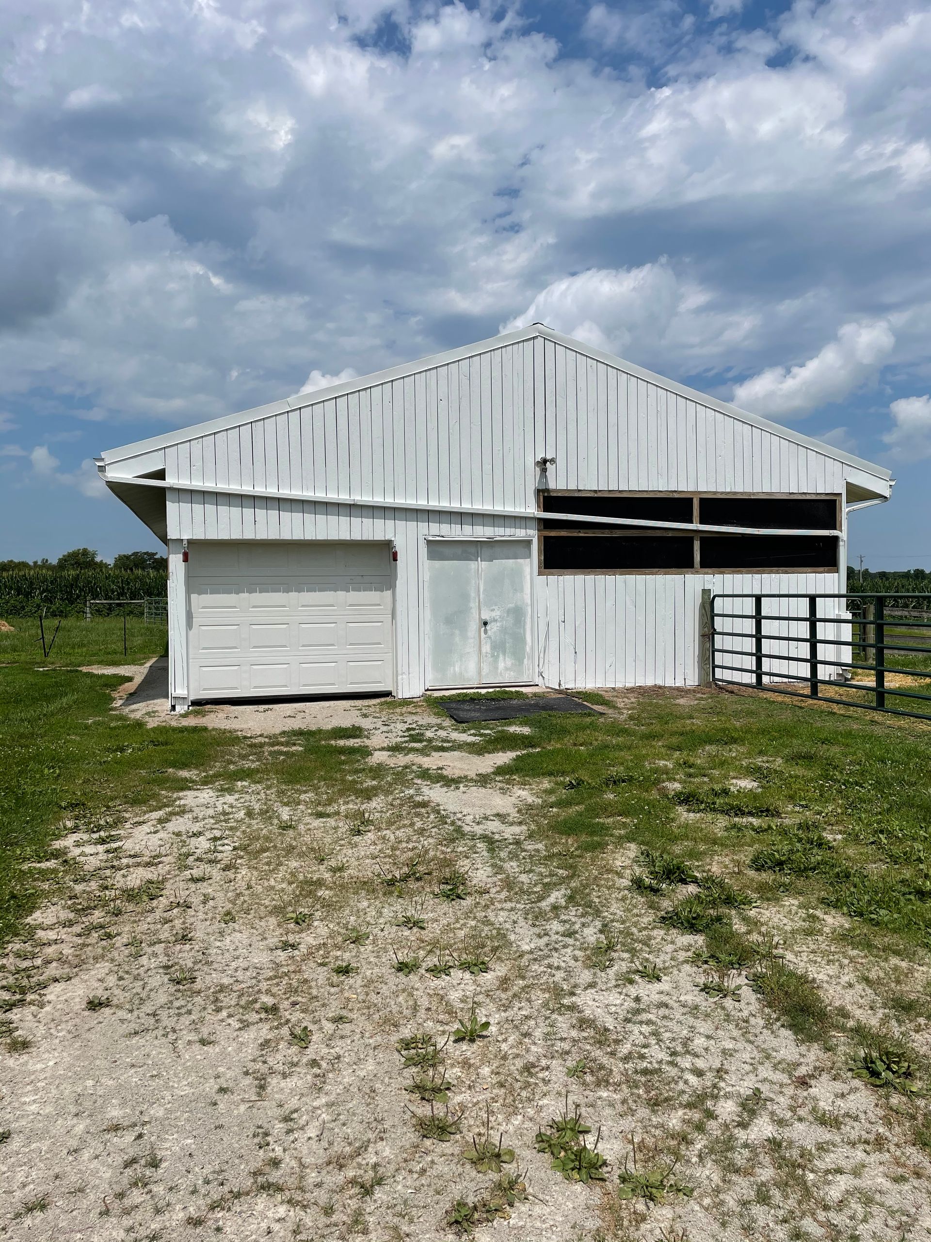 A white barn with a garage door is sitting in the middle of a grassy field.